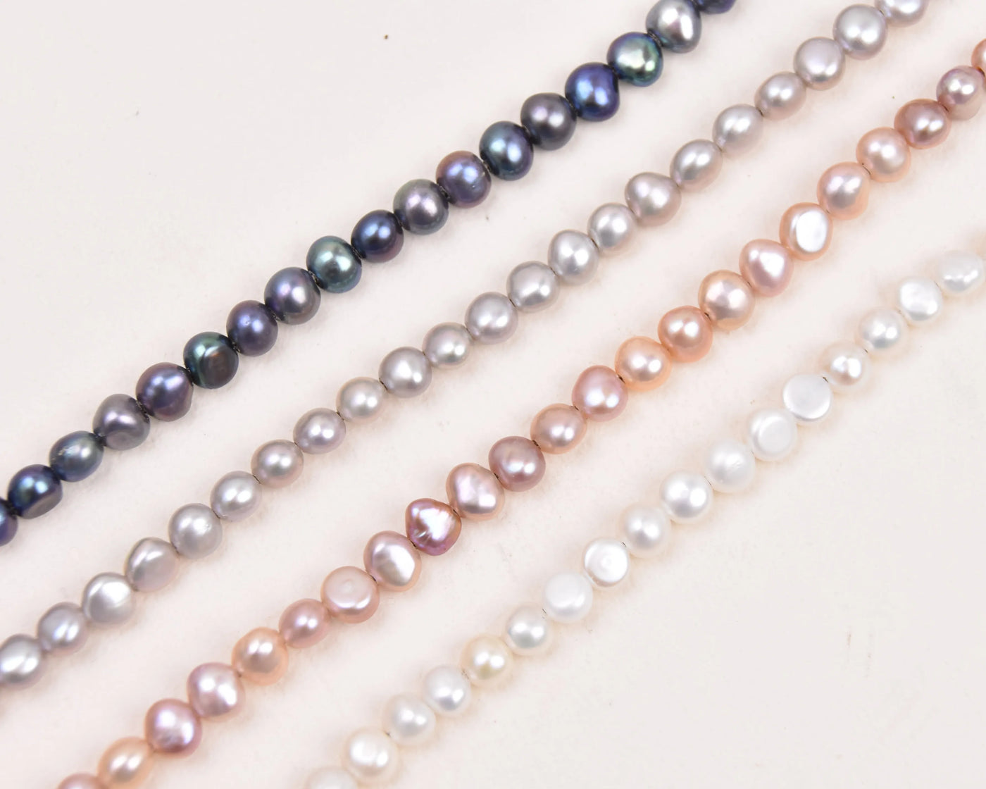 Peacock, Silver, Blush and White pearls in diagonal lines on a white background