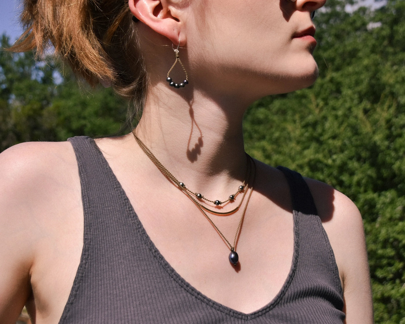 Dripping in Pearls necklace stack with earrings in peacock on model with trees in background