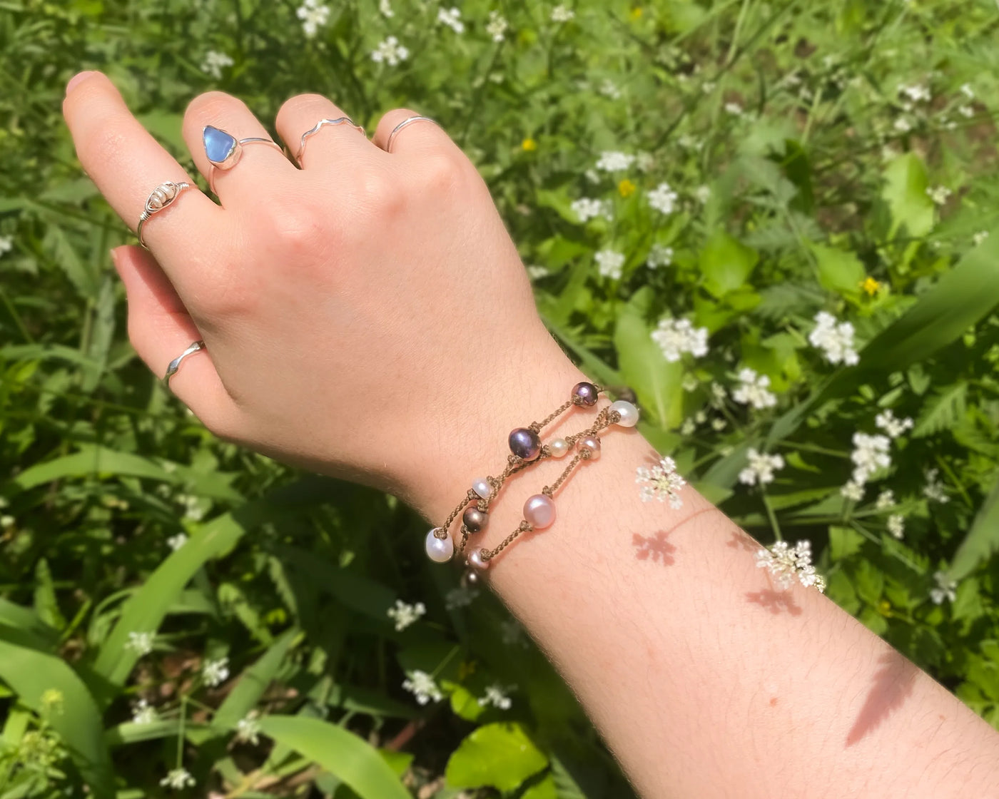 Tula Blue's Journey Bracelet in mixed pearls on model wrist in front of greenery