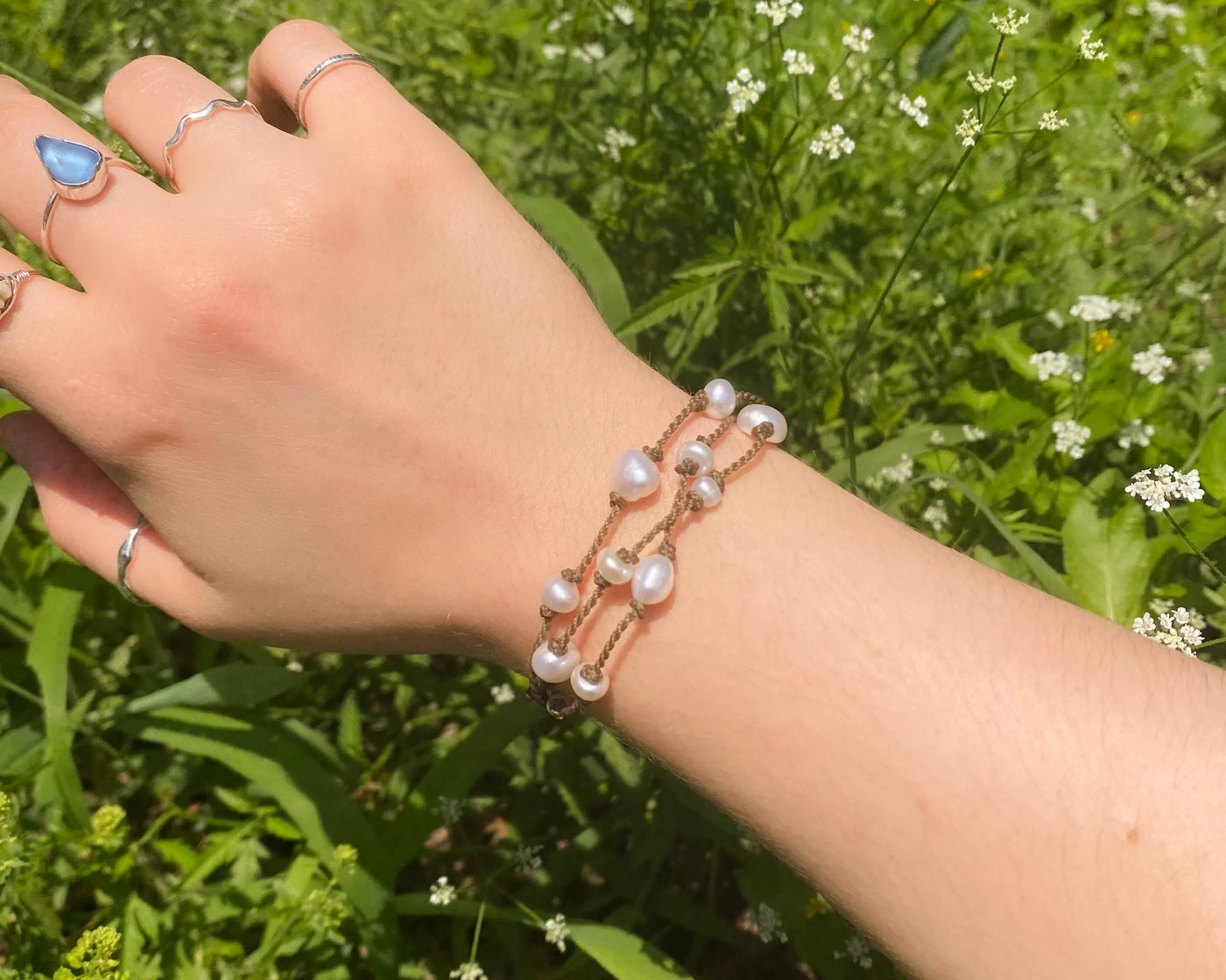 Tula Blue's Journey Bracelet in white pearl on model wrist in front of greenery