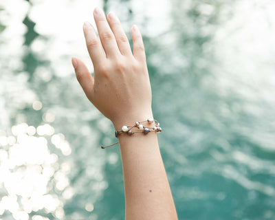 Tula Blue's Journey Bracelet in mixed pearl on model wrist and hand in front of water