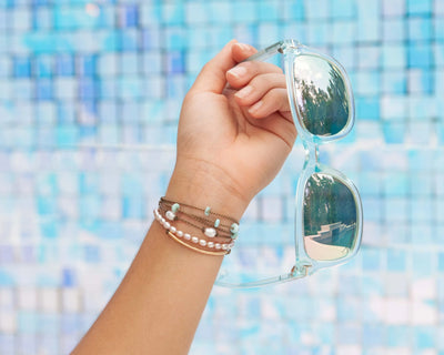 sunlit lagoon bracelet stack on model holding a pair of sunglasses with blue background