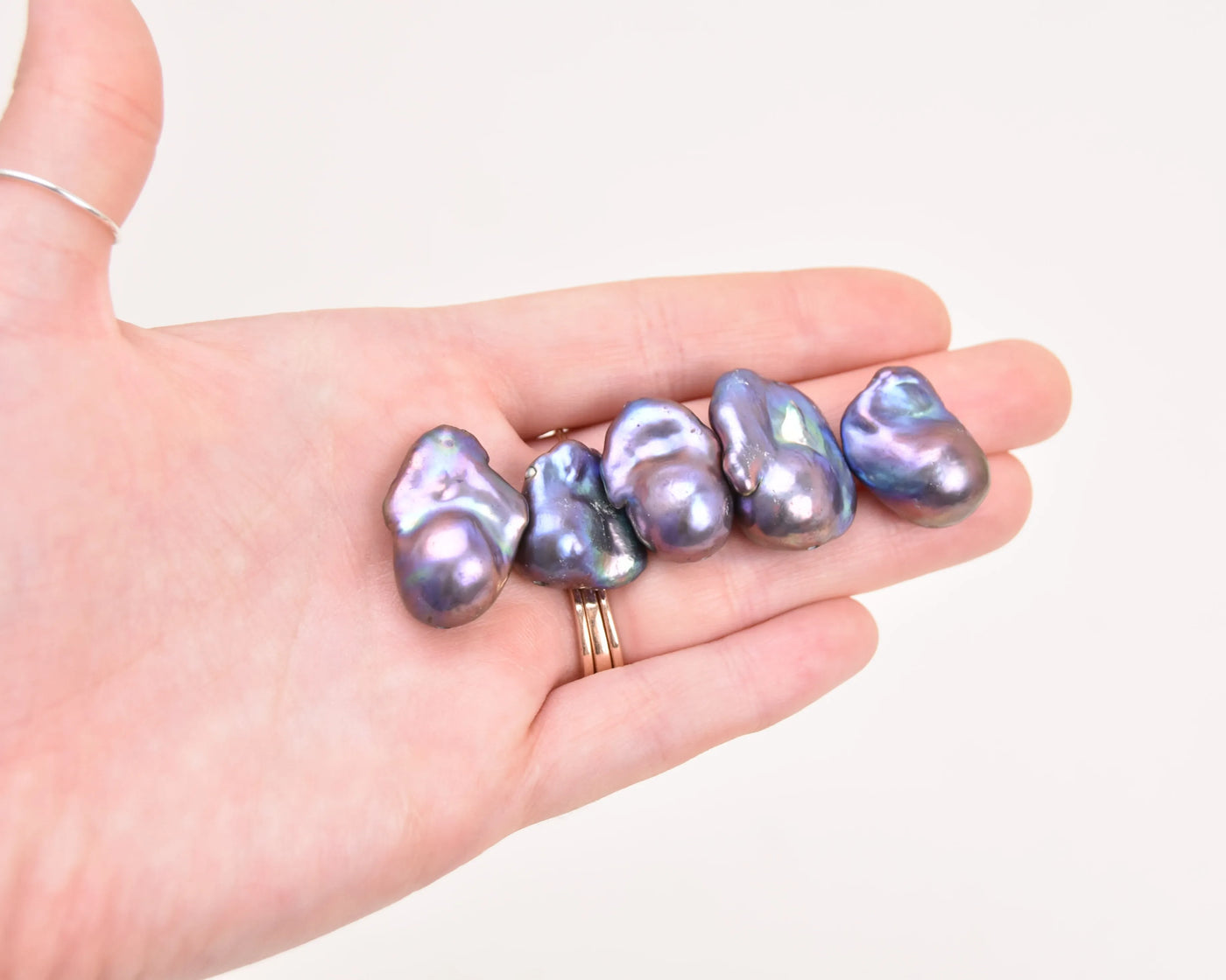 Five Peacock Flame Keshi Pearls on their own in the palm of a hand to show the variations and unique shapes of the pearls