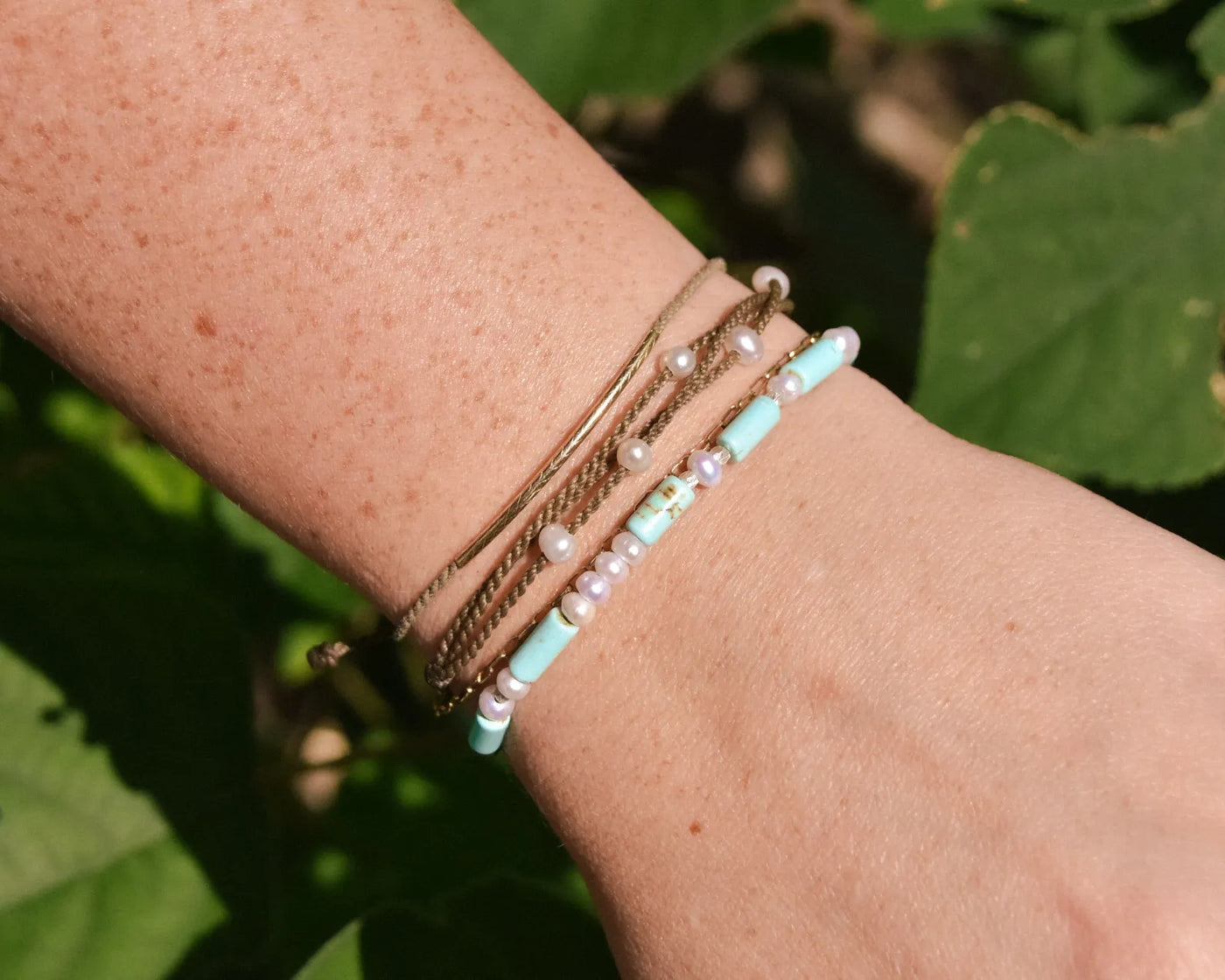 Turquoise, Pearl and Sterling Silver bracelet mixed with other bracelets on model wrist as a closeup in front of greenery