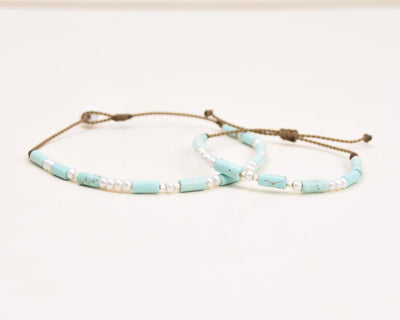 Turquoise, Pearl and Sterling Silver anklet and bracelet stacked on top of each other viewed at an angle on white background