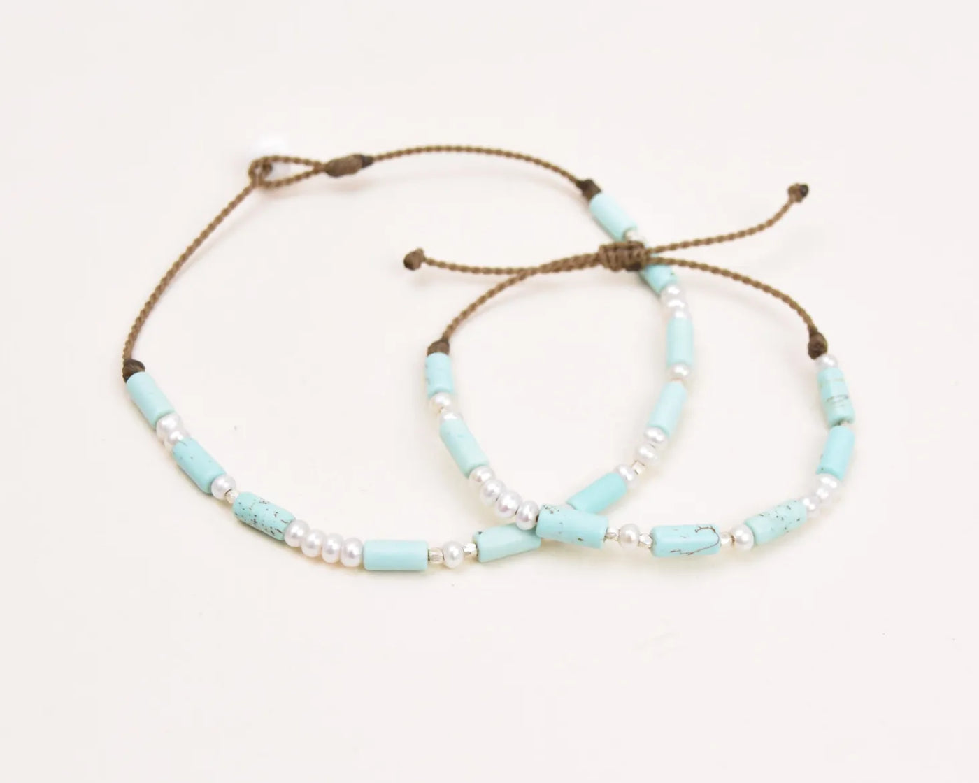 Turquoise, Pearl and Sterling Silver anklet and bracelet stacked on top of each other viewed from a top down angle 